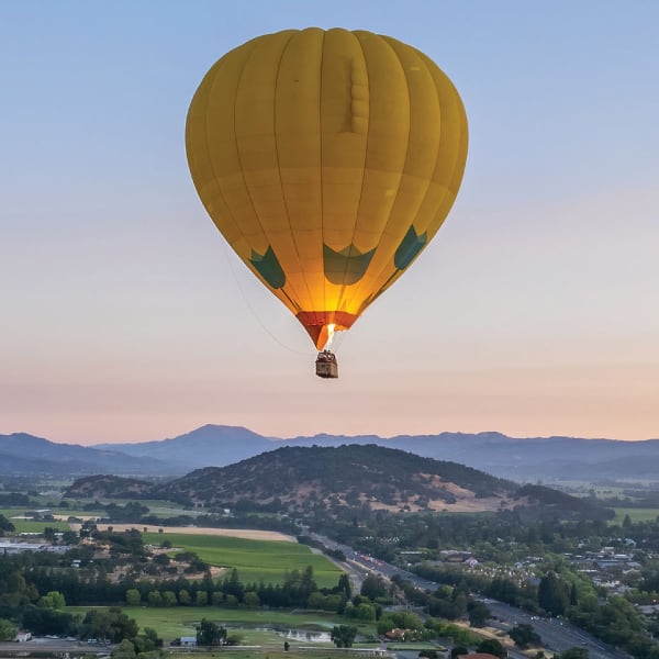 A hot-air balloon glows in the early morning dusk as it floats over Napa Valley