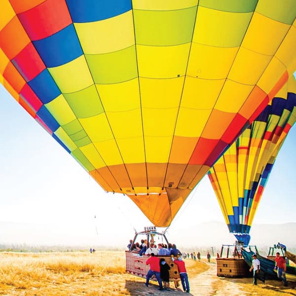 Crews assist on the ground as hot-air balloons land in a grassy field
