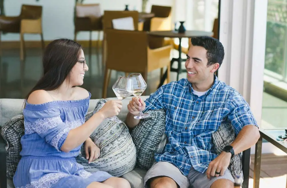 A couple seated on a comfy patio loveseat raises wine glasses in a toast.