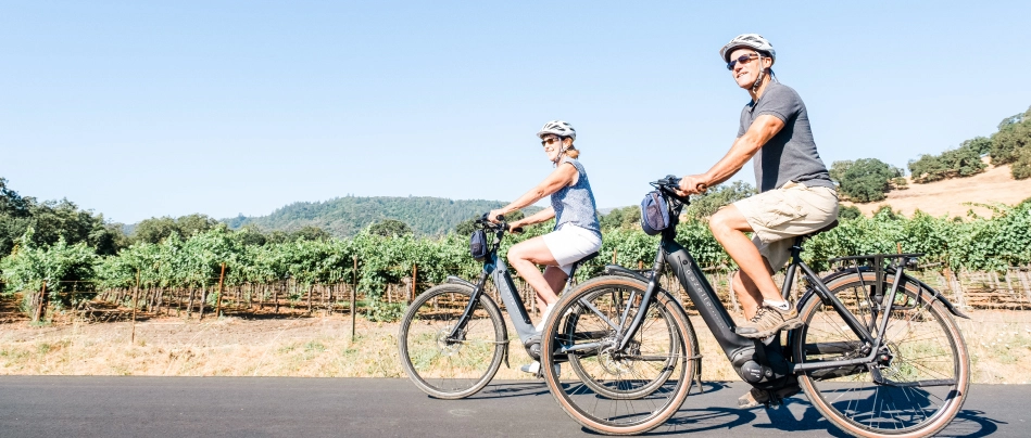 A couple rides electric bikes past the vineyards