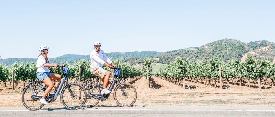 A couple rides electric bikes past the vineyards in Napa Valley