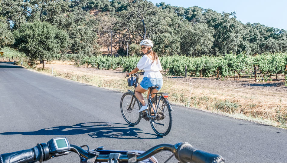 A woman rides an electric bike ahead of her partner and looks back over her shoulder at them