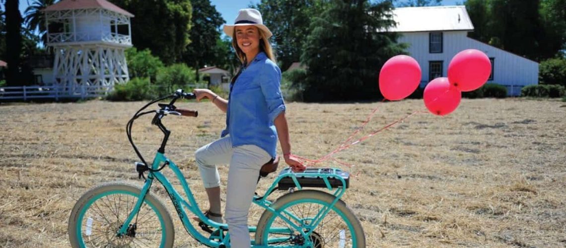 A woman poses with an electric bike with a Napa Valley winery in the background