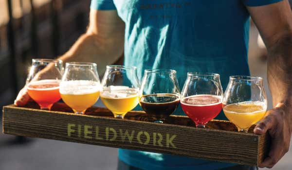 A server carries a wooden box tray with a tasting flight of six beers.