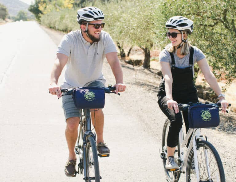 A couple smiles and laughs while biking next to each other on a guided bike tour through Napa Valley.