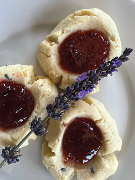 Three lavender jam thumbprint cookies with a fresh sprig of lavender