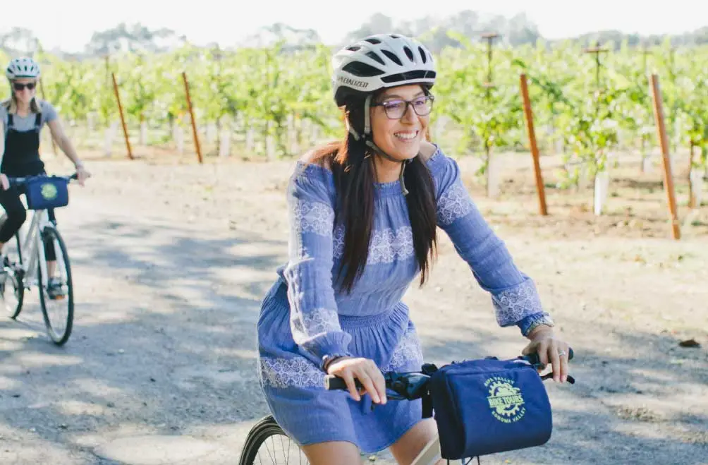 A woman smiles while riding a bike along a road with vineyard views.
