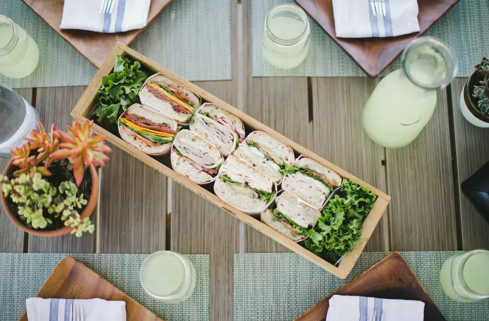 Overhead view of a tabletop setting including a platter of deli sandwiches.