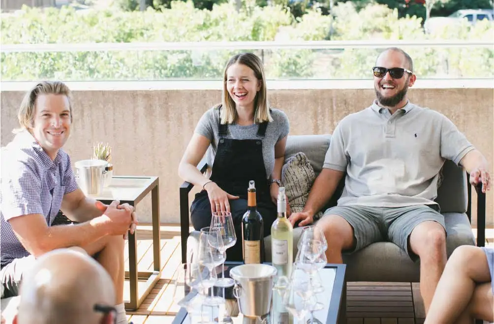 Three people smile while holding wine glasses and enjoying an outdoor patio wine tasting.