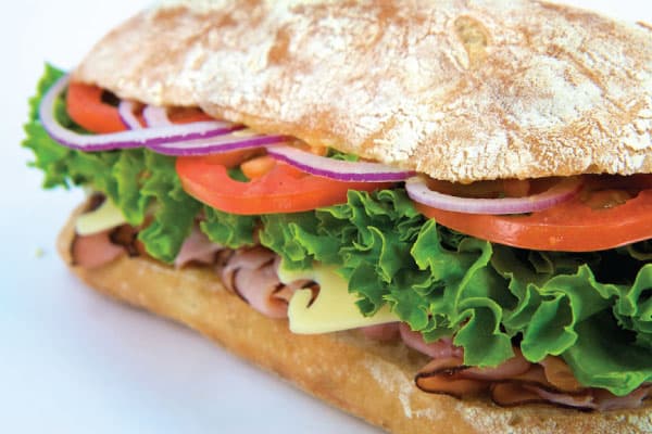 Close up of a deli sandwich with lettuce, tomato, red onion and cheese