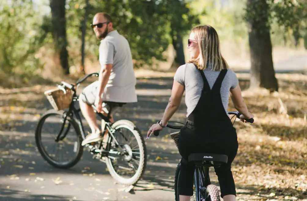 A couple rides cruiser style bikes along a car-free bike path.